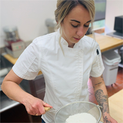 Audrey Anderson. White woman in chef's jacket sifting flour into a bowl. 