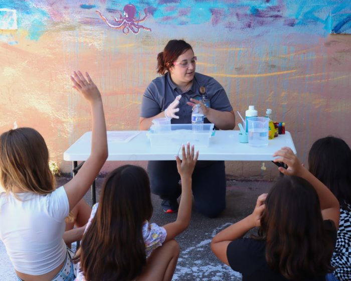 four female students raising their hands while observing a chemistry demonstration of elephant toothpaste.