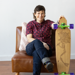 Portrait of Katherine Edmonds presenting a long board she made to the camera