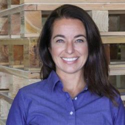 QSL Printing Communications CEO, Melissa Koke, standing in front of a wall of wooden palettes in a portrait photo.