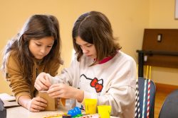 Two sisters working together to build a cardboard structure to test on a shake table."